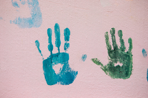 Blue and green coloured handprints on a pink wall