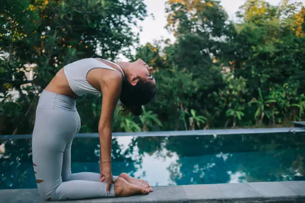 Photo of Young fit woman relaxing in Camel pose during yoga practice at poolside