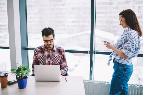 istock Smart casual man and woman using cellphone and laptop technology for sharing files connected to bluetooth in office, Caucasian employees searching application for making online booking and banking 1407272423
