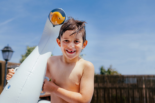 Summer vacation concept. Portrait Caucasian smiling cute child with no on tooth holds swan inflatable ring. Kid having fun outdoors, in a pool of a private house backyard.