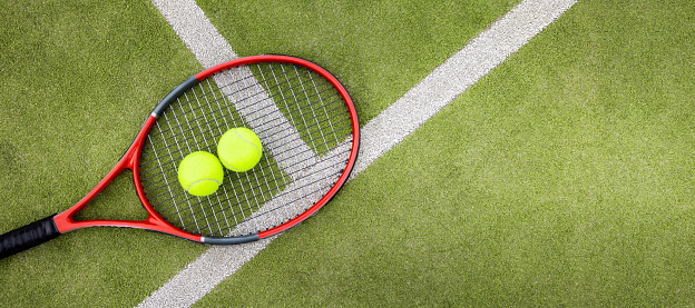 tennis balls and racket on green synthetic grass court background. top view with copy space