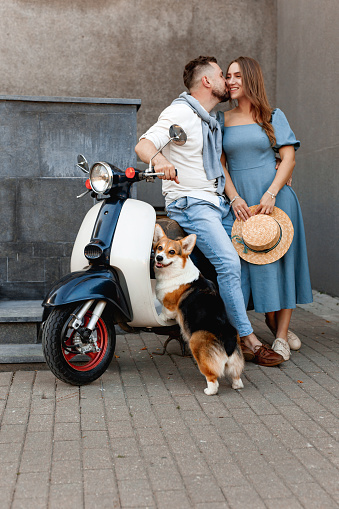 Happy beautiful couple with dog on scooter in old european city