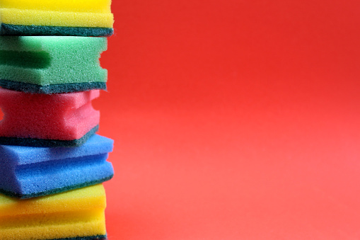 Multi-colored bright sponges for washing dishes stand on a red background.
