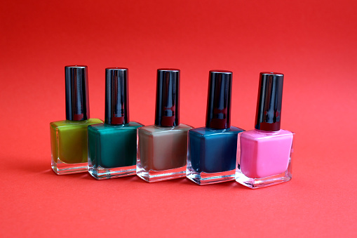 Several colors of nail polishes stand on a red background.
