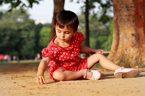 Small girl playing with soil outdoor in public park.