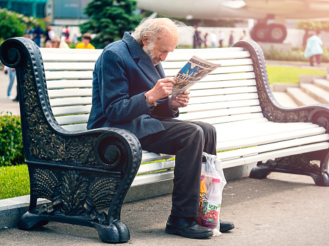 An elderly man sits on a park bench and reads a newspaper. Moscow Russia 18.06.2022