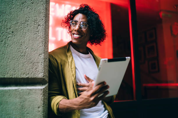 istock Smiling ethnic man using tablet on city street 1407277170