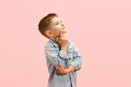 Portrait of little boy, child in jeans t-shirt posing isolated over pink background. Dreaming look. Concept of childhood, family, emotions, lifestyle, fashion. Copy space for ad, flyer