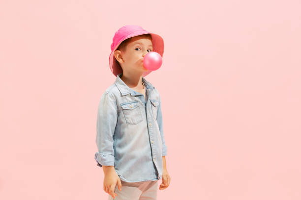 porträt eines süßen kleinen jungen, eines kindes in jeans-t-shirt und panamas, das mit kaugummi über rosa hintergrund isoliert posiert - ethnic small fashion model one person stock-fotos und bilder