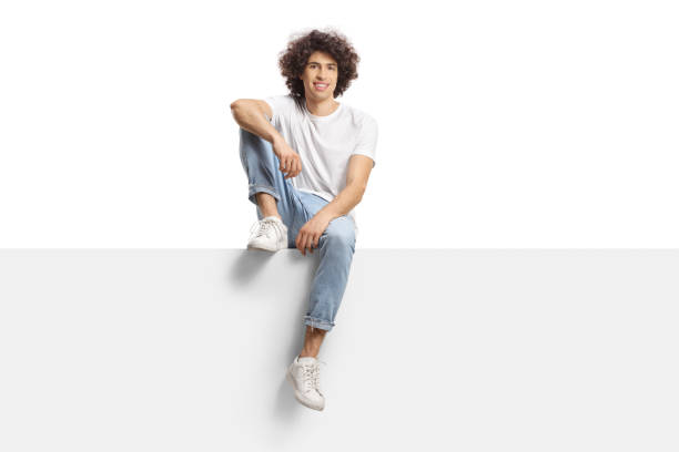 istock Casual young man with curly hair sitting on a blank panel 1407279886