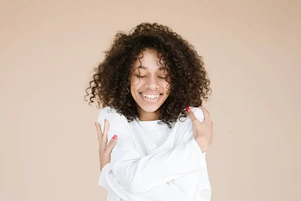 Photo of smiling african american girl holding hands on shoulders wear casual white t-shirt isolated beige background