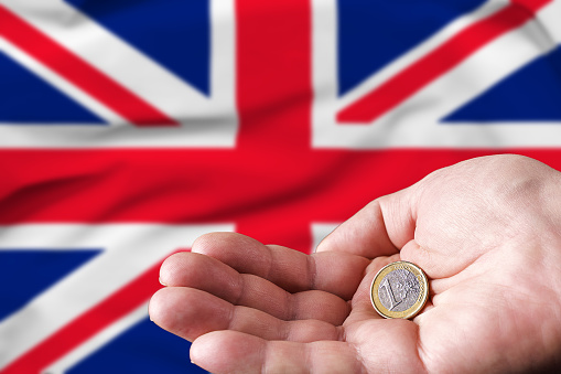 Coin one euro in the hand of a man, the flag of Britain on the background.