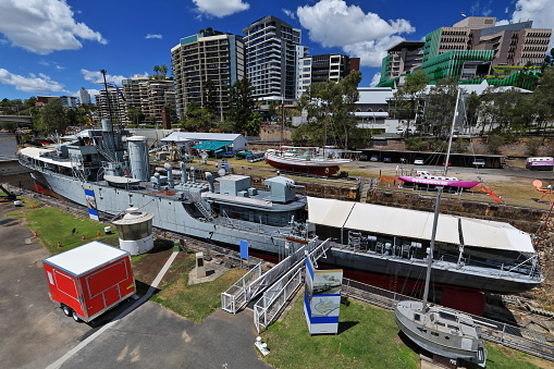 Ships berthed at South Brisbane dry dock: river-class frigate, Torres-Strait pearling lugger-bright pink sail yacht. Modern apartment buildings in background. South Bank-Brisbane-Queensland-Australia.