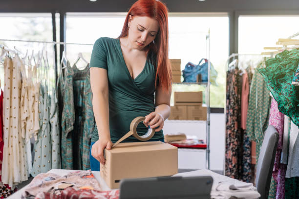 young business woman, closing a cardboard box with adhesive tape, order for customer of her online clothing shop. young woman preparing a package for a client in the office. work and business concept. - sales clerk store manual worker retail imagens e fotografias de stock