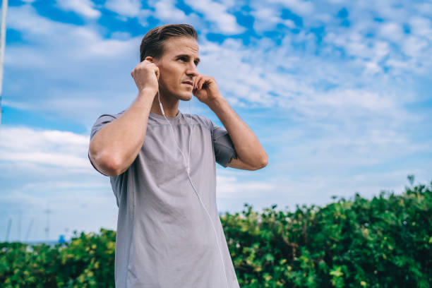 esportista musculoso caucasiano usando fones de ouvido eletrônicos se preparando para a corrida matinal, fisiculturista alethic 30 anos de idade em fones de ouvido modernos ouvindo discos de som e playlist de música - 25 30 years audio - fotografias e filmes do acervo