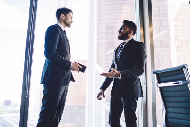 istock Diverse colleagues dressed in elegant suit communicate near panoramic window in corporate office, multiracial male partners 30 years old discussing productive collaboration and brainstorming briefing 1407284181
