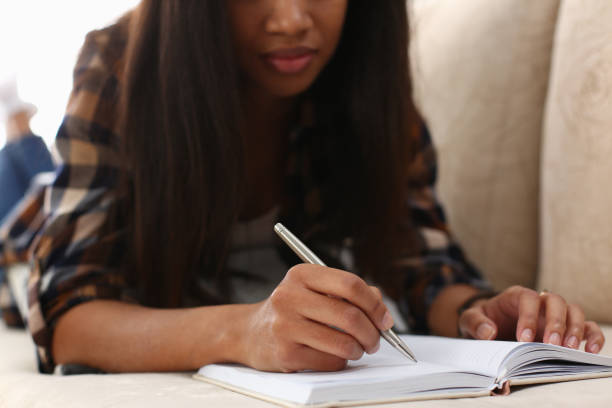istock Afro american woman with open journal, writing in personal diary, chill on couch 1407284897