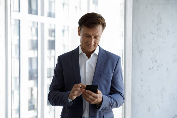 istock Middle-aged businessman standing in office, check messages on smartphone 1407285172