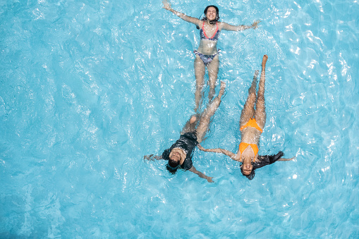 Three women in bikinis floating in a sunny summer swimming pool