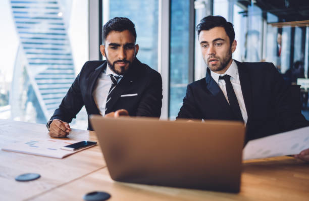 istock Male company employees using laptop computer for research useful information on financial platform for business people, skilled executive managers collaborating on web project discussing ideas at desk 1407285376