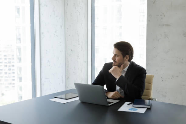 istock Businessman sit at desk with laptop staring aside looking thoughtful 1407285678