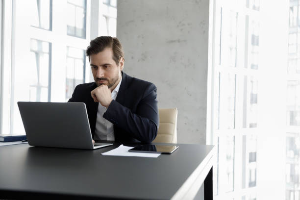 istock Serious focused businessman using laptop working seated at modern office 1407285679