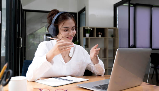 istock Smiling young asian woman in headset wave greet talking on webcam virtual conversation on laptop, happy female in wireless headphones speak on video call on computer, consult client online 1407285748