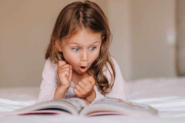 Fantasy literature. Emotional child girl read interesting book in bed. Small kid enjoy reading. Fantasy and fantastic. Developing child fantasy and imagination. Imaginary world. Fairy tale. Bedtime reading literatura fantástica. niña emocional leyó un libro interesante en la cama. los niños pequeños disfrutan de la lectura. fantasía y fantástico. desarrollar la fantasía y la imaginación infantil. mundo imaginario. cuento de hadas. lectura antes de a