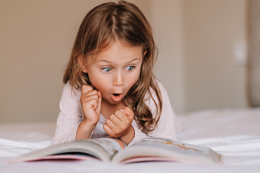 Fantasy literature. Emotional child girl read interesting book in bed. Small kid enjoy reading. Fantasy and fantastic. Developing child fantasy and imagination. Imaginary world. Fairy tale. Bedtime reading
