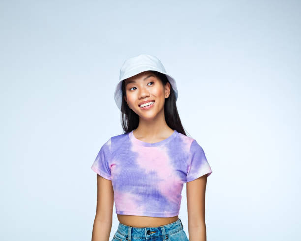 Young woman in lilac tie dye top Portrait of young woman wearing lilac tie dye top and white bucket hat, looking away and smiling. Studio shot against blue background. bucket hat stock pictures, royalty-free photos & images