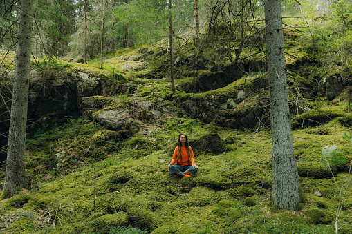 Female traveler in orange enjoying a day in the scenic Swedish forest, meditating on the soft moss