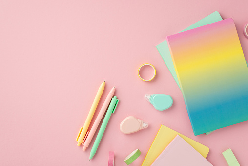 School accessories concept. Top view photo of colorful stationery rainbow color diary pens round correction tape ruler and adhesive tape on isolated pink background