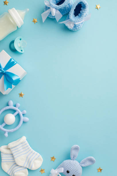 istock Baby concept. Top view vertical photo of giftbox shoes socks pacifier teether milk bottle knitted bunny rattle toy and gold stars on isolated pastel blue background with copyspace 1407292019