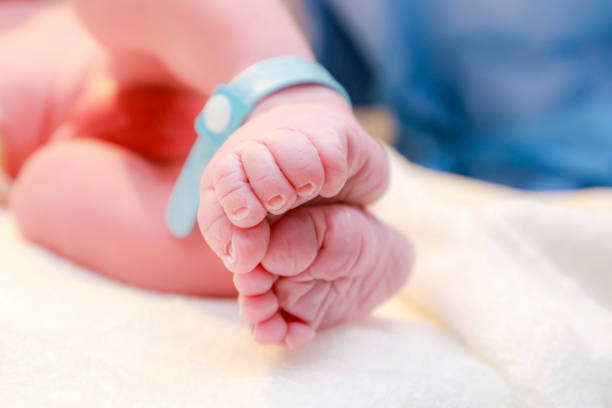 Newborn baby feet in hospital bed lying on their back with hospital bracelets on his feet Newborn baby feet in hospital bed lying on their back with hospital bracelets on his feet baby bracelet stock pictures, royalty-free photos & images
