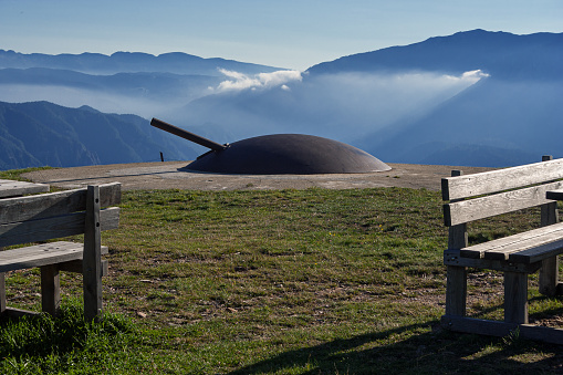 Armored dome of the Busa Granda Fort in Trentino, with a cannon howitzer, against the background of the Mountains and the Brenta Group