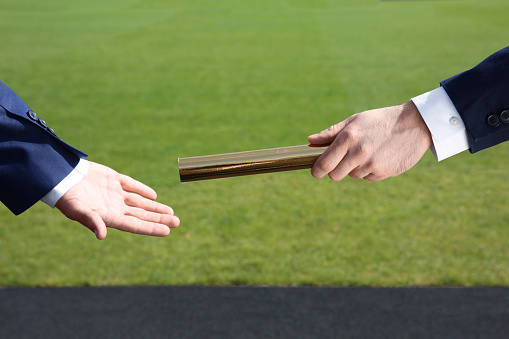 Businessman passing baton to his partner outdoors, closeup