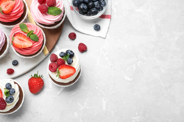 istock Sweet cupcakes with fresh berries on light marble table, flat lay. Space for text 1407301233