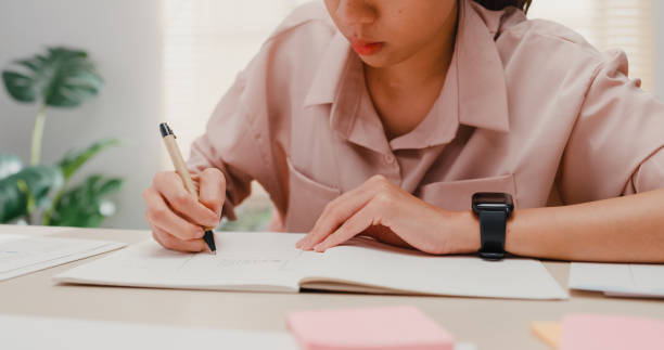 close up tangan wanita muda asia menulis di buku catatan saat bekerja di kantor. - education potret stok, foto, & gambar bebas royalti