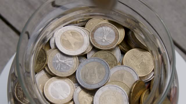 Euro coins being poured in glass jar in slow motion
