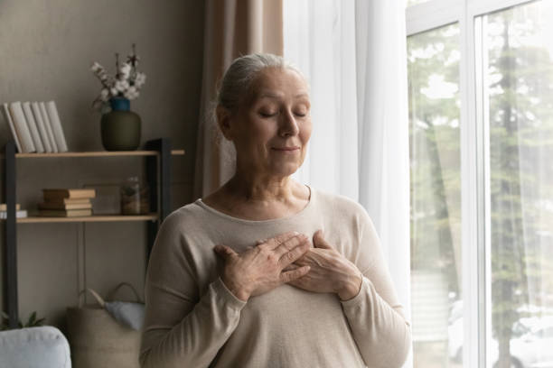 istock Peaceful older female with folded palms on chest standing indoor 1407303665