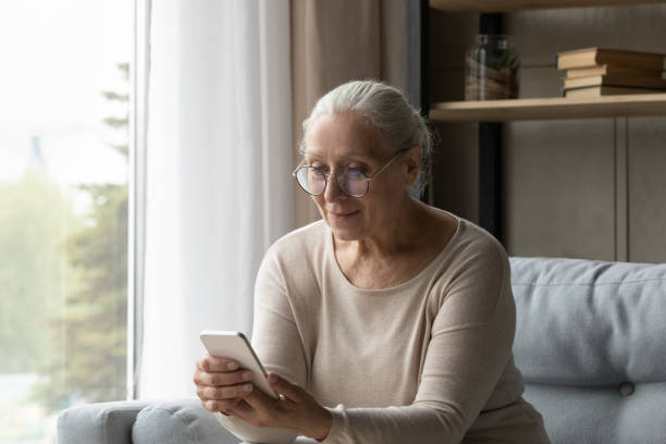 istock Aged woman use smartphone seated on sofa at home 1407303674