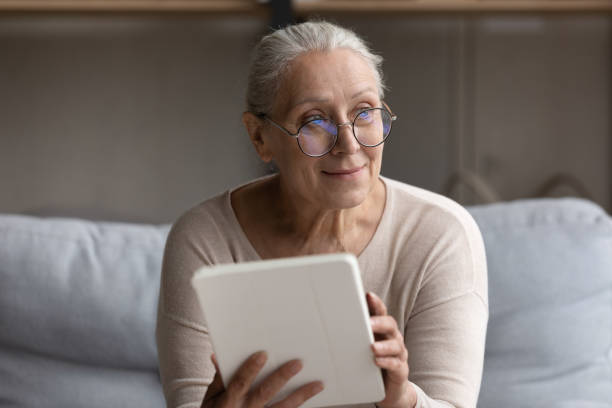 istock Smiling older woman in eyeglasses holds digital tablet staring aside 1407303689