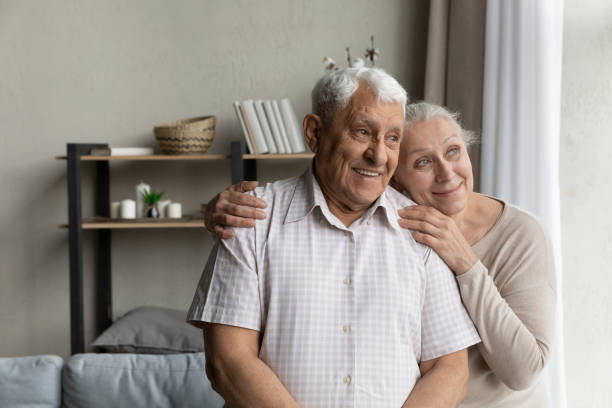 elderly loving couple standing in living room looking out window - 96 well imagens e fotografias de stock