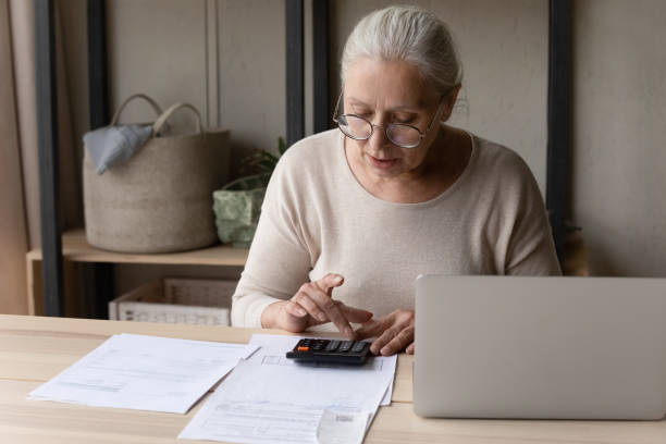 istock Older woman sitting at table using calculator manage personal budget 1407303720