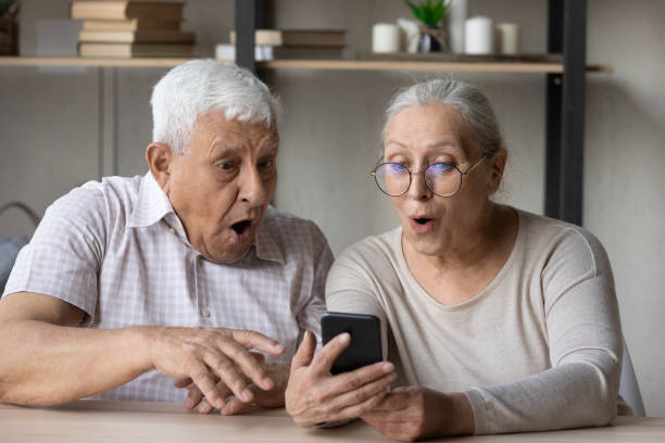Grandparents open mouth gawp at cellphone screen, read unbelievable news Older couple open mouth gawp at cellphone screen, get unbelievable, fantastic commercial, profitable offer seated at table indoors. Read great news, opportunity, moment of online lottery win concept gawp stock pictures, royalty-free photos & images