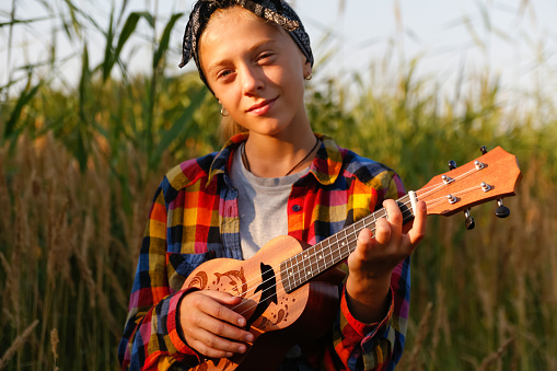 Defocus girl with guitar. Teen girl walking on nature background. Little kid girl outside on green meadow. Generation z. Summertime. People musician. Smiling fashion kid. Singer. Out of focus.