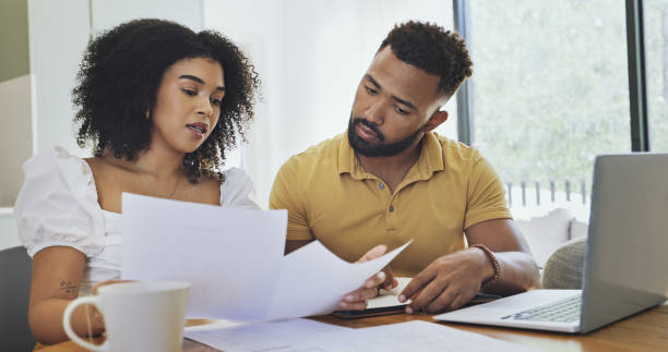 istock Couple reading documents and paying bills using a laptop at home. Husband and wife planning their budget and finances. Man and woman working on their savings. Girlfriend and boyfriend doing taxes 1407308477