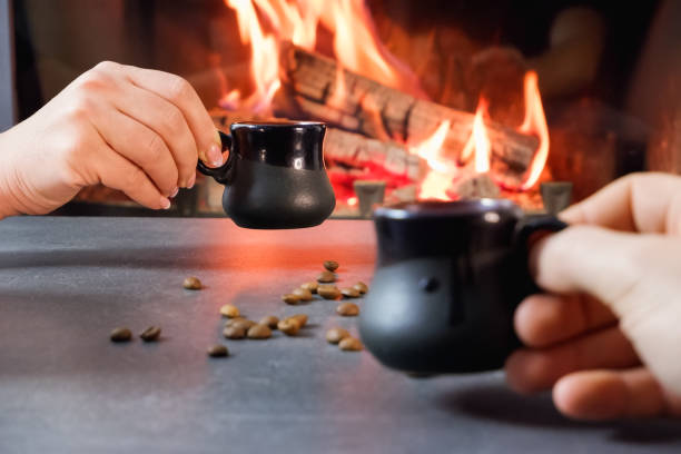 istock Romantic coffee break. A couple drinks coffee from ceramic coffee cups against a backdrop of burning fire and coffee beans. Close-up on hands. 1407309369