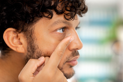 Side view, close up of a young male adult applying a contact lens wearing casual clothing