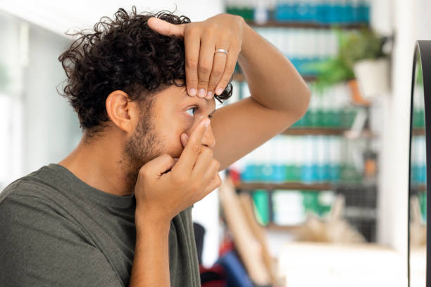 Contact Lens Application Side view medium shot a young male adult applying a contact lens looking in a vanity mirror wearing casual clothing. contact lens stock pictures, royalty-free photos & images